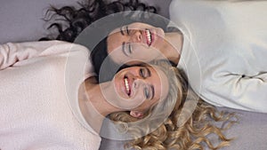 Beautiful ladies with blond and dark hair lying on floor and sincerely laughing