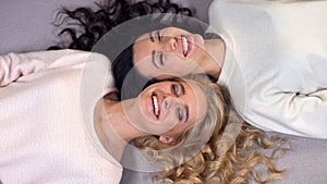 Beautiful ladies with blond and dark hair lying on floor and sincerely smiling