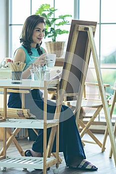 Beautiful lady Asian woman sitting and use a brush to pain picture in the room. Idea for hobby, relaxation or artist work from