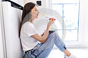 Beautiful young woman in casual clothes tasting delicious chocolate while sitting on the floor in the domestic cuisine