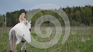 beautiful lady dressed like bride is riding white graceful horse, romantic shot at field