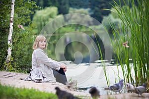 Beautiful lady feeding pigeons on a lake shore