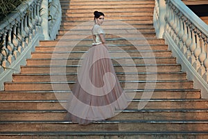 Beautiful lady in luxurious ballroom dress walking up the stairs of her palace