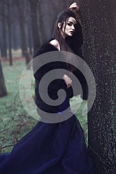 Beautiful lady in luxurious sequin evening dress and sable fur coat standing in the mysterious misty woods