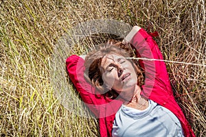 Beautiful lady lying down in dry summer field to enjoy sun