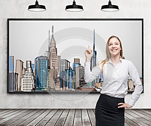 A beautiful lady is pointing out the picture of New York City on the wall. Wooden floor, concrete wall and three black ceiling lig