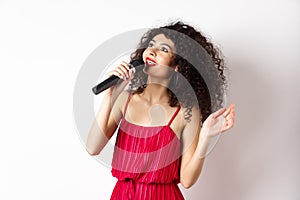 Beautiful lady in red dress singing songs in microphone, smiling and looking up, standing on white background