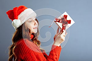 Beautiful lady in Santa hat is holding presents, looking at camera and smiling, isolated on gray background