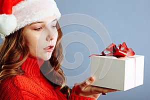 Beautiful lady in Santa hat is holding presents, looking at camera and smiling, isolated on gray background