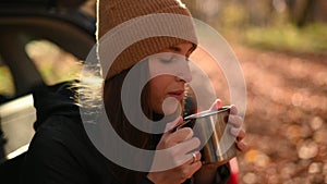 Beautiful lady sitting in open car trunk and drink tea or coffee