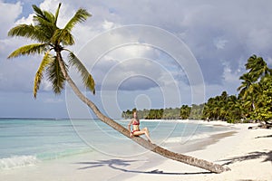 Beautiful lady is sitting on the palm tree at tropical beach photo