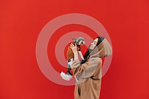 Beautiful lady standing on a red background with a cute dog breed biewer terrier in her arms and smiling. Woman with pet in her