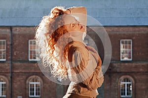 Beautiful lady with sunlight highlighting cascading long wavy red hair, hand holding hair on top of her head