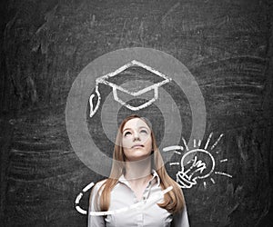 Beautiful lady is thinking about education. A graduation hat and a light bulb are drawn on the chalkboard above the lady.