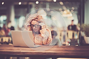 Beautiful lady use personal laptop computer sit down on a bar wooden table with other people defocused in background - digital