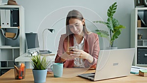 Beautiful lady using smartphone touching screen smiling sitting at desk in office