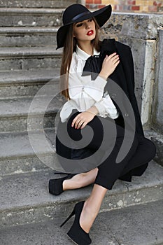 Beautiful ladylike woman in elegant clothes sitting on stairs in park