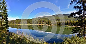 Beautiful lake high in the mountains surrounded by forest. Blue sky, white clouds.