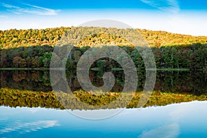 Beautiful lake with reflection of forested hill in the calm water