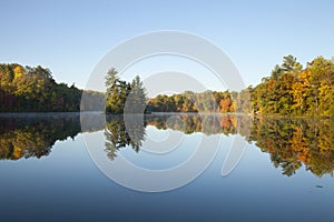 Beautiful lake with trees in autumn color and a small island in northern Minnesota on a calm clear morning