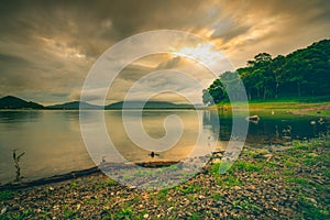 Beautiful landscape of Bang Pra reservoir in the morning with sunrise above the mountain and green tree forest. Cloudy sky