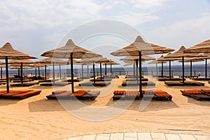 Beautiful landscape of beach with wooden sun beds, thatched umbrellas