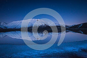 Beautiful landscape in Castelluccio di Norcia during a frozen night on Mount Redentore reflected in the lake, Umbria, Italy