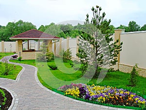 Beautiful landscape design in a private yard. Colorful flowers, green grass and trees. Cosy barbeque house / grill house. Beautifu