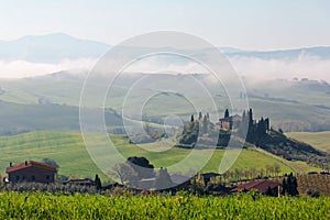 Beautiful landscape of farmhouses on the green grassy fields over rolling hills in idyllic Tuscan countryside