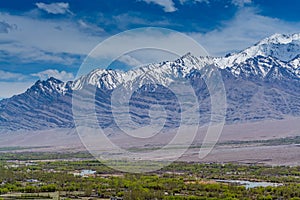 Beautiful landscape with fields of delta of Indus River, Tibetian buildings, Himalayas snow mountains, and blue sky,  in Ladakh,
