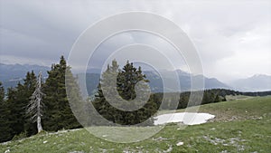 Beautiful landscape with green forested hill with high mountains in clouds on the background. Action. Foggy rocks and