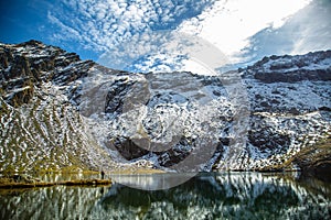 Beautiful landscape with high snowy rocks, lake in which the mountains are reflected, blue sky with white clouds and one man