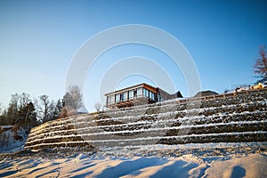 Beautiful landscape with a house on a cliff and a stone wall and fence in winter with snow and sun during sunset or