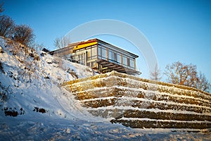 Beautiful landscape with a house on a cliff and a stone wall and fence in winter with snow and sun during sunset or