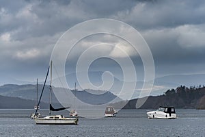 Beautiful landscape image of leisure boats on Lake Windermere in Lake District during overcast Spring afternoon with mountain