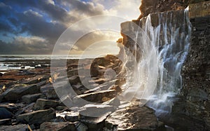 Beautiful landscape image waterfall flowing into rocks on beach