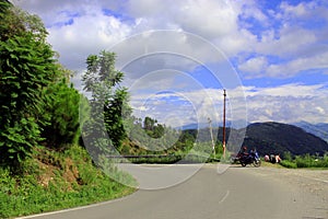 Beautiful landscape with mountains, twisting road, forest and pines,blue sky clouds and bike parked on roadside