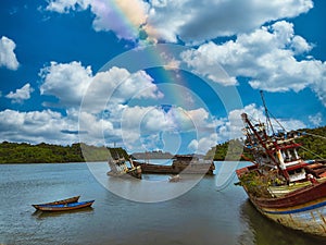 Beautiful landscape of old ships in the sea under a blue cloudy sky with a rainbow.