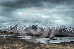 Beautiful landscape over the calm lake with the snowy mountains in the background on a gloomy day