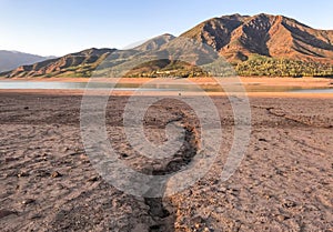 Beautiful landscape with setting sun: mountains, lake and cracked earth - dried-up riverbend. Copy space
