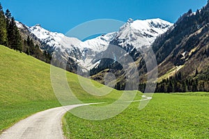 Beautiful landscape with snow capped mountains, green grass meadows and hiking trail in springtime. Trettachtal, Allgaeu