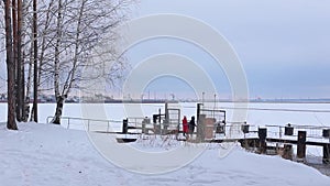 Beautiful landscape of snow-covered shore with trees and river pier on which comes couple in love and looks at white frozen river