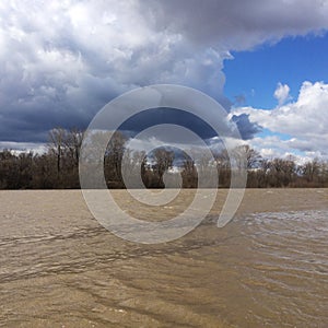 Beautiful landscape of the spring flood of river, stormy stream of dark water mixed with clay and blue sky in clouds