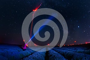 Beautiful landscape of a starry night with milky way and blue sky over a field of lavender and red lights of wind turbines