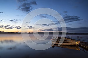 Beautiful landscape sunrise over still lake with boats on jetty