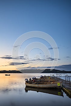 Beautiful landscape sunrise over still lake with boats on jetty