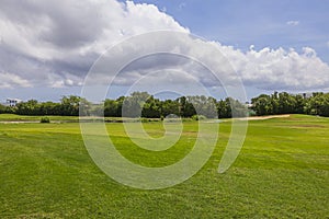 Beautiful landscape view of green grass golf field on green trees and blue sky with white clouds background. Aruba.