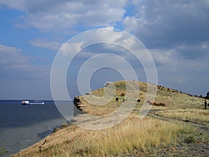 Beautiful landscape with a view of a herd of cows on a cliff and a cargo barge floating on the river on a clear autumn day