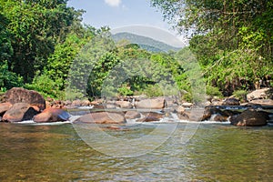 Beautiful landscape view of small waterfall in the river with water stream flowing through stone and green trees in the background