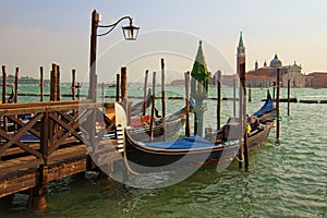 Beautiful landscape view of Venetian Lagoon. Moored gondolas near wooden pier. San Giorgio Maggiore church at the background.